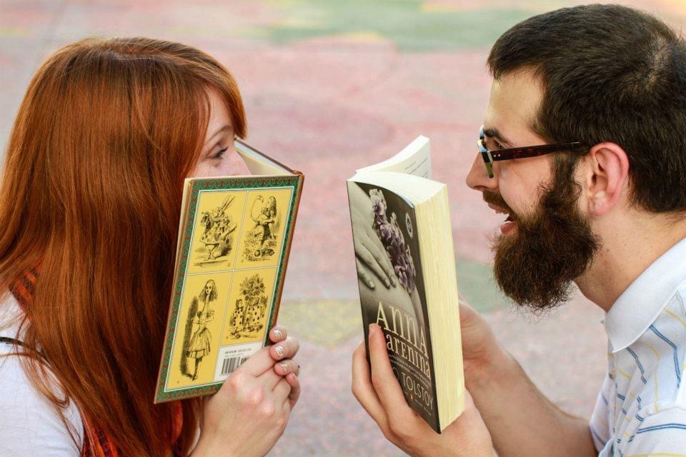 Joe and Sarah peering over the tops of two books to look at each other. Joe is laughing. Sarah's face is hidden from the nose down.